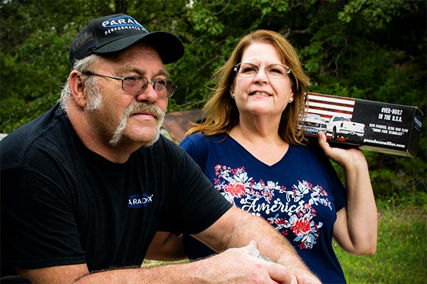 The owners of Paradox Performance Muffler pose with a muffler while wearing an American flag shirt