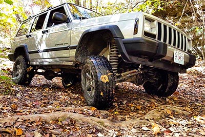A Jeep Grand Cherokee with a Paradox Performance Muffler driving on a leaf-covered forest trail.