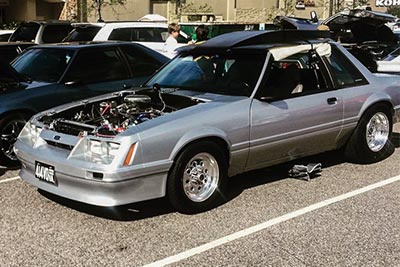 A silver Ford Mustang Fox Body with Paradox Performance Mufflers at a car show.