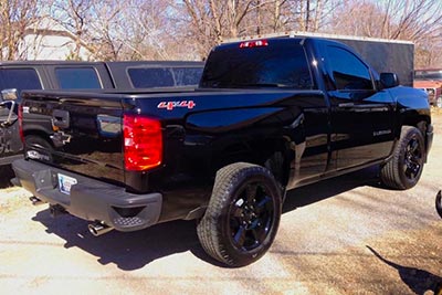 A black Chevy Silverado 1500 with the exhaust drone eliminating and deep sounding Paradox muffler. The truck is parked outdoors on a paved lot, shown from a rear three-quarter angle.